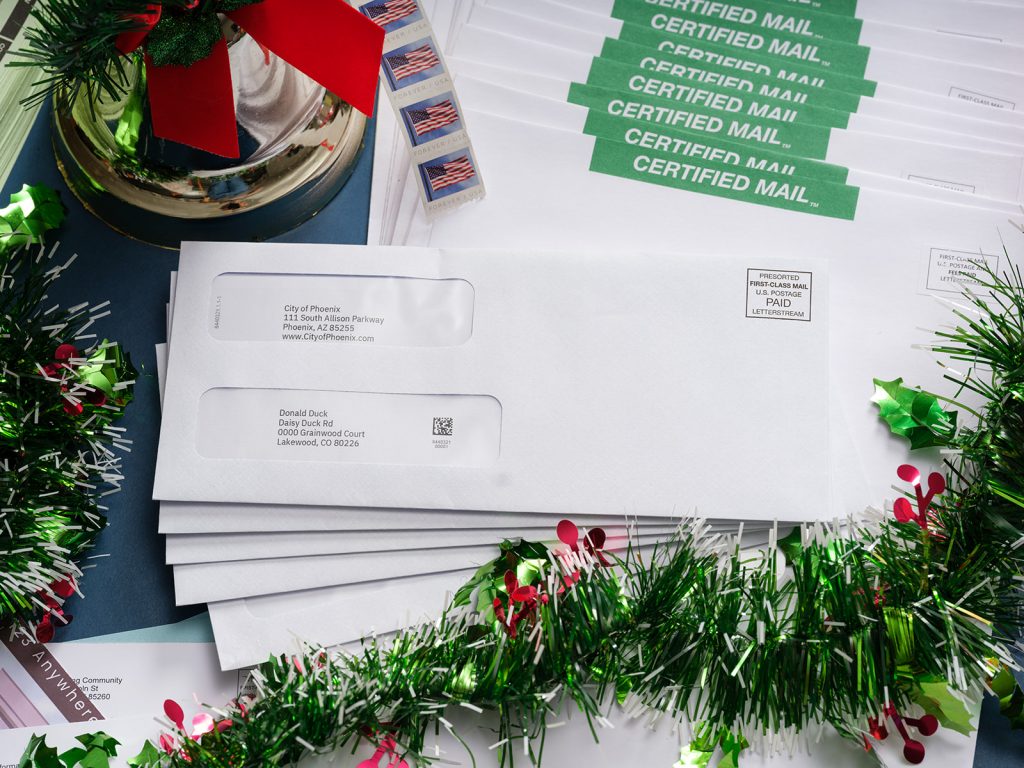 First-class mail on top of Certified Mail envelopes with Christmas decor around it for usps holiday mail