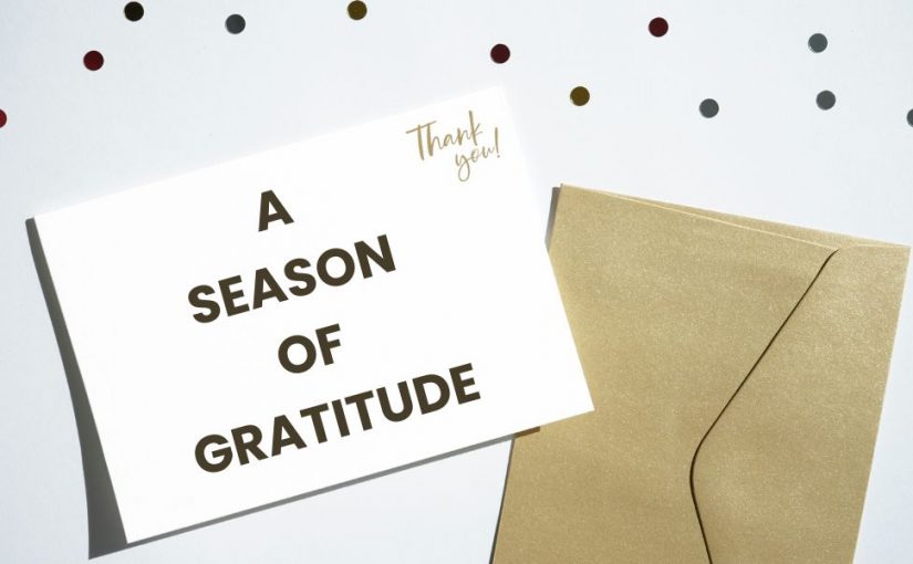 A card that says a season of gratitude on it on top of a gold envelope for printing and mailing company
