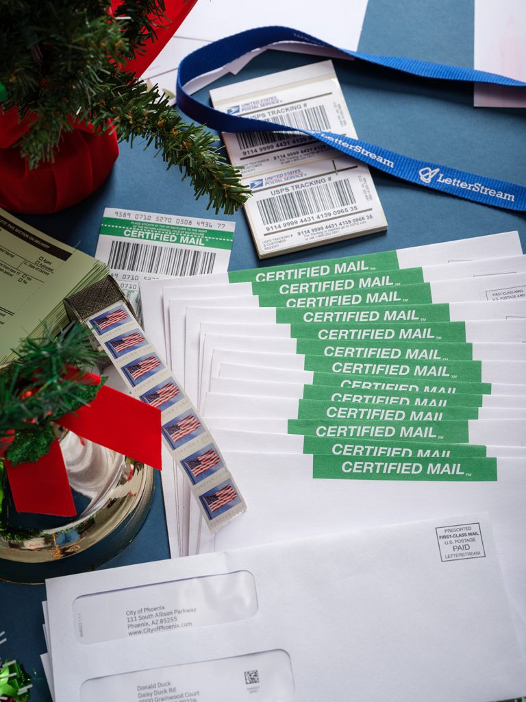 Part of Christmas tree branch and a Christmas bell located next to a LetterStream lanyard with Certified Mail envelopes and Certified Mail tracking and USPS stamps